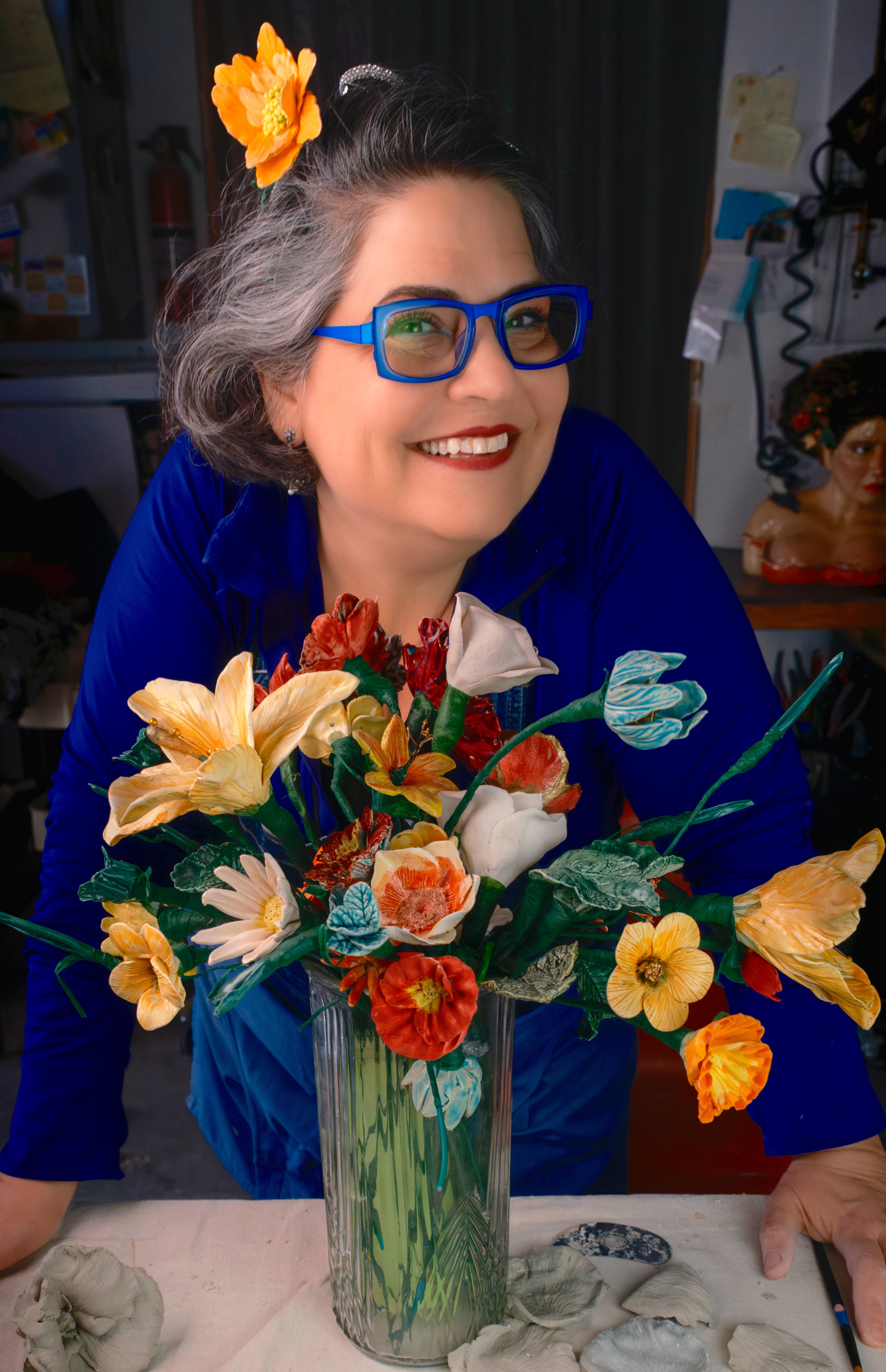 1.Bernadette Esperanza Torres in blue glasses with her handmade ceramic flowers in a vase in her art studio_Photo Credit Stone Addams