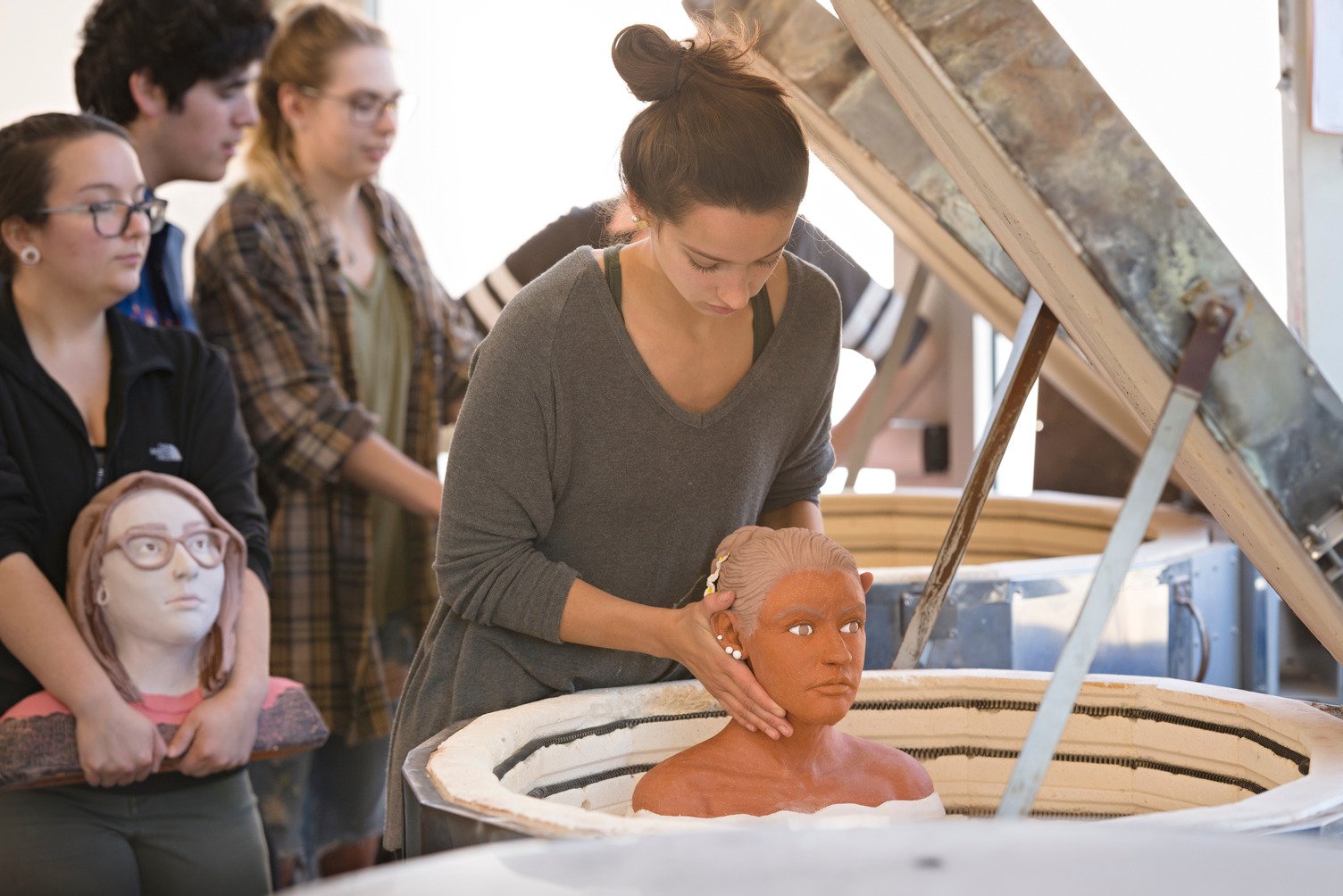 KCAI ceramics student lowers ceramic bust into on-site Richard J. Stern ceramic studio kiln