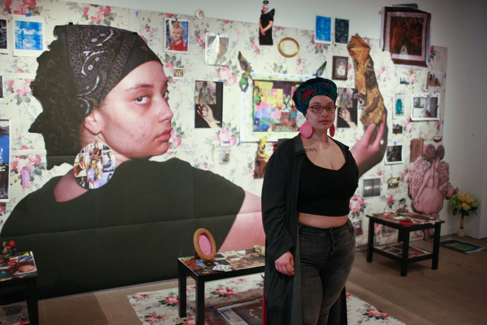 KCAI Student poses in front of their art on display in the H&R Block Artspace