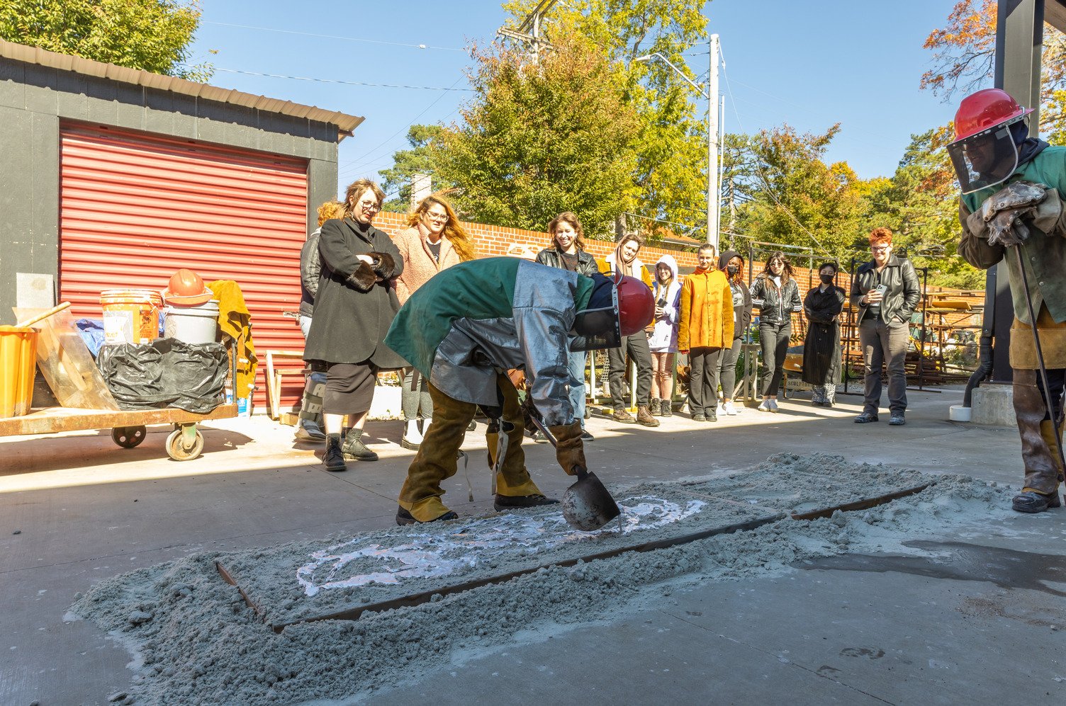 Students watch as artists work with molten metals outside the William Volker Sculpture Studio