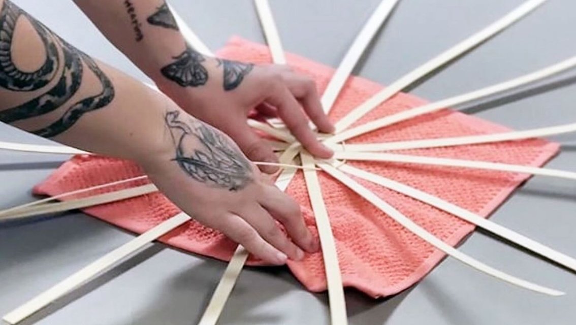 Hands weave a basket on a salmon-colored towel